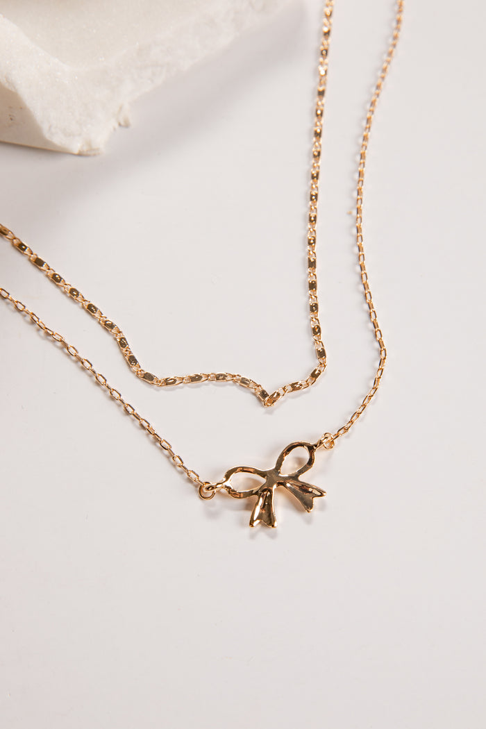 Gold necklace with a bow pendant on a light background