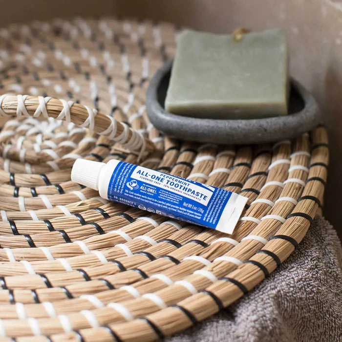 Tube of All-One toothpaste on a woven mat with soap in the background