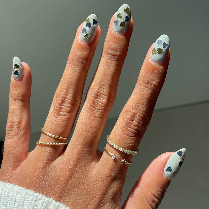 Hand with almond-shaped nails painted with light polish and decorated with silver and gold hearts using Biggest Fan polish