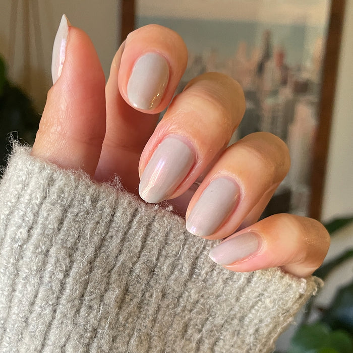 Hand with soft natural skin tone nails painted in iridescent milky grey Elevator quick dry polish for at home mani