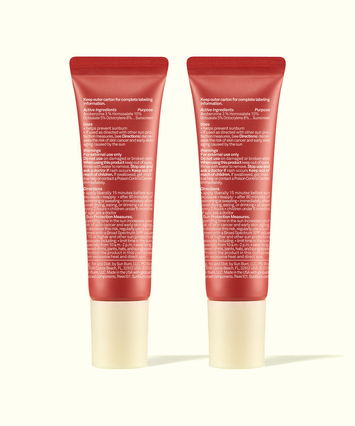 Two red tubes of Sun Bum Tinted Lip Duos standing side by side with white caps showing product directions.
