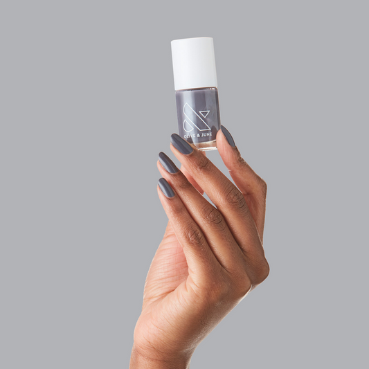 Hand holding Olive and June 100% CHANCE nail polish with nails painted in gunmetal blue shade for a long-lasting mani