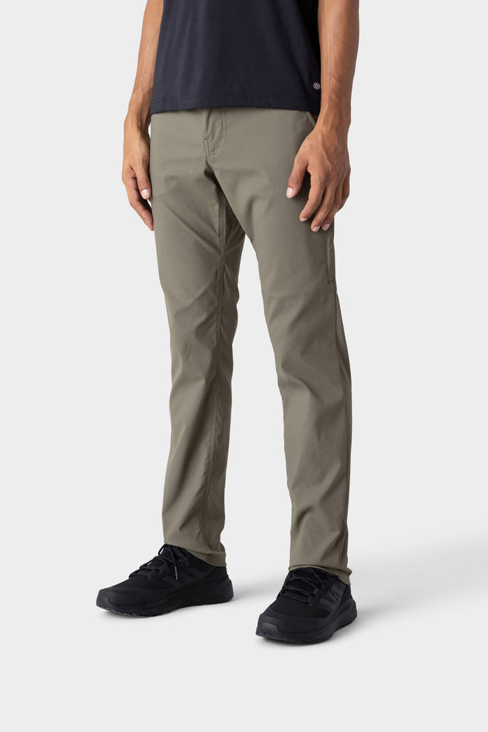 A person wearing 686 Mens Everywhere Merino-Lined Pant - Slim Fit in olive green, paired with a black T-shirt and black sneakers, stands against a light gray background. Only the lower half is visible‚Äîperfect for staying warm in colder weather.