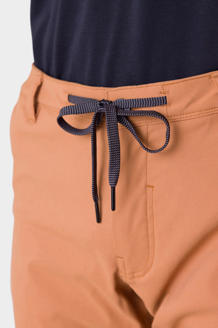 Close-up of a person wearing 686 Mens Everywhere Pant - Slim Fit in light orange with a dark blue drawstring, paired with a dark navy top.