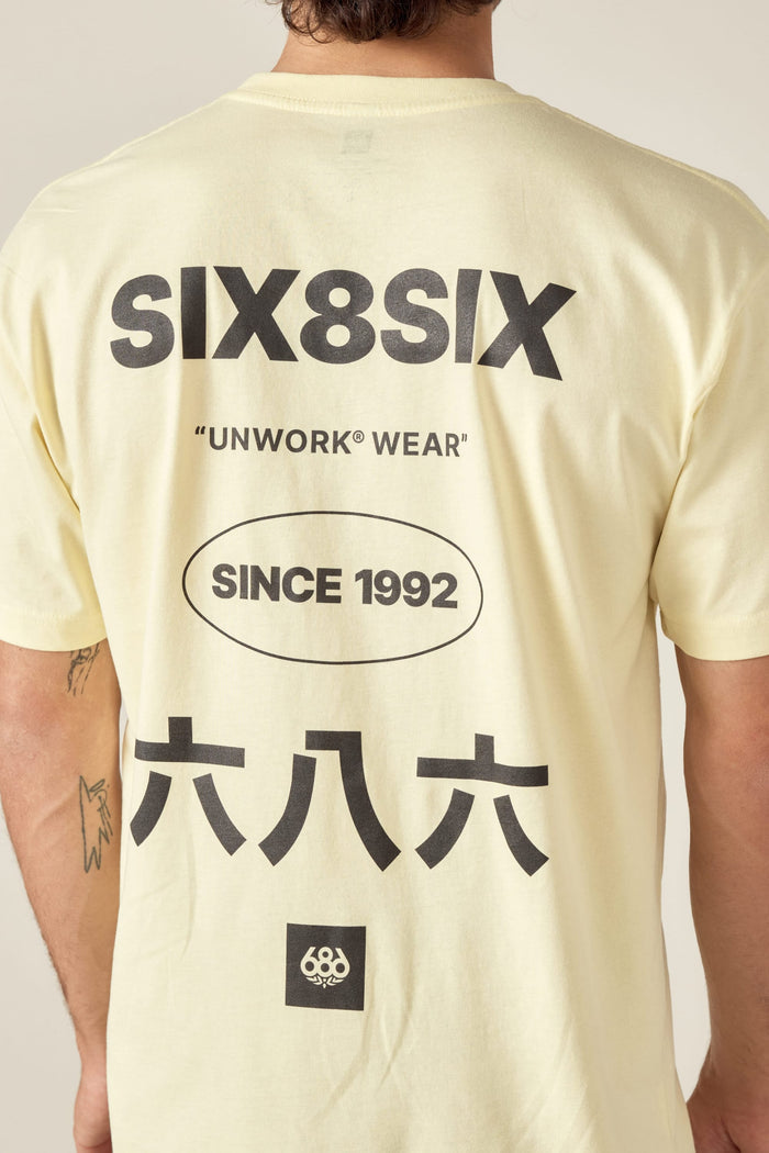 A man wears the 686 Unwork Wear Authentic S/S Tee by 686‚Äîa light yellow, 100% cotton shirt with bold black SIX8SIX, UNWORK® WEAR, SINCE 1992 text, Japanese characters, and a small circular logo on the back.