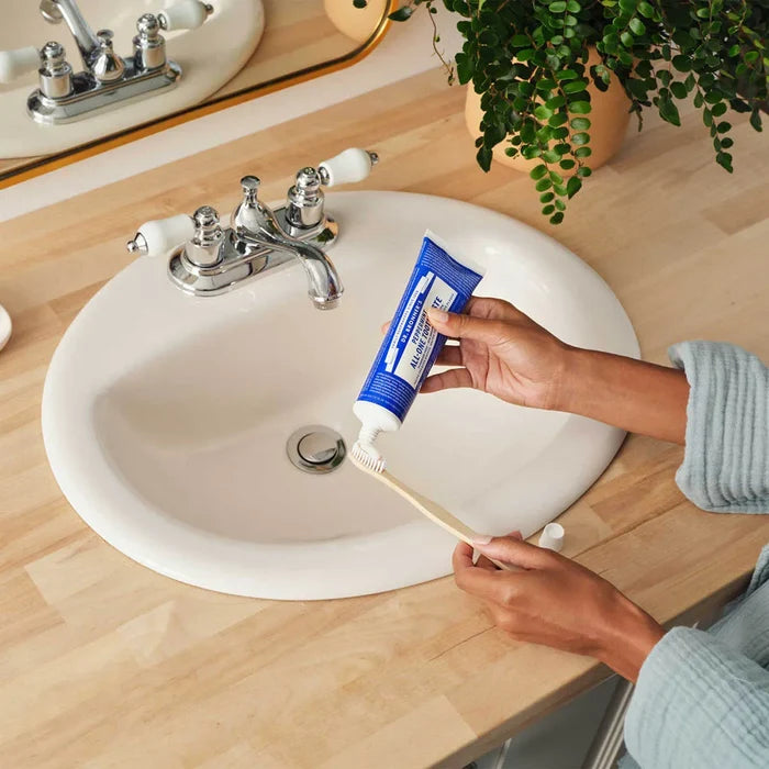 Person applying toothpaste to a toothbrush in front of a sink.
