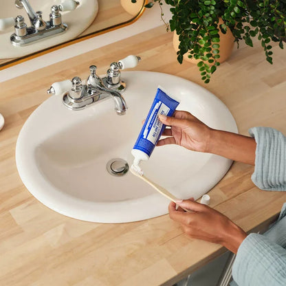 Person applying toothpaste to a toothbrush in front of a sink.