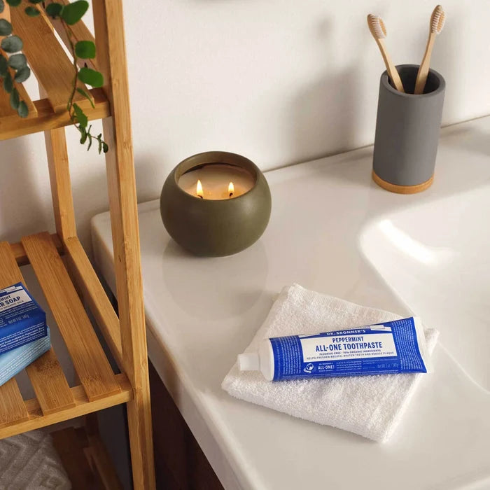 Bathroom counter with a tube of toothpaste, towel, and candle on a wooden shelf.