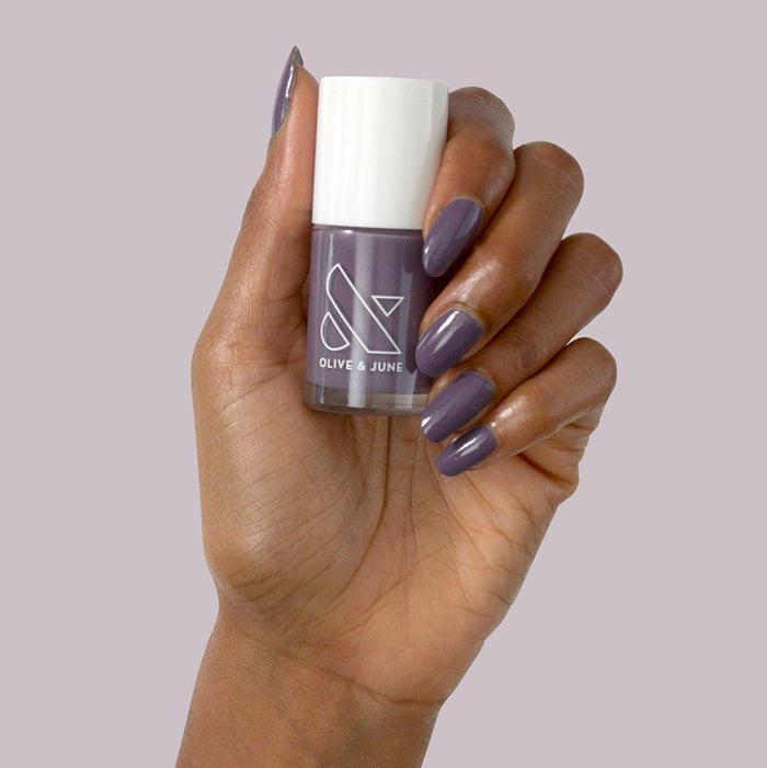 Hand holding Art Class polish with smooth, glossy muted eggplant manicure against a soft purple background