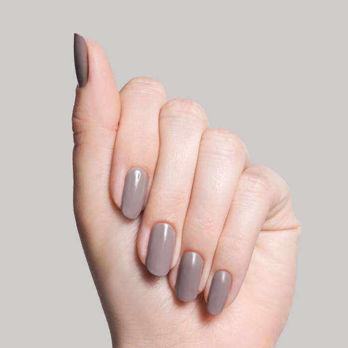Hand with nails painted in AW warm grey shade showing a smooth, glossy manicure against a light grey background