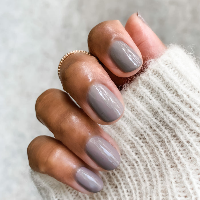 Fingers with nails painted in AW showing a smooth, glossy manicure against a soft textured neutral background