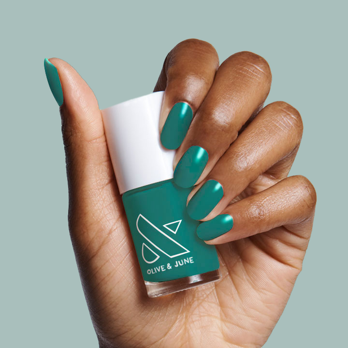 Hand with nails painted deep emerald green shade Besties holding Olive and June polish bottle for a smooth mani