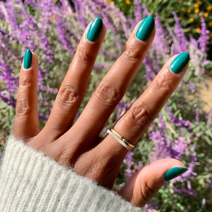 Hand with nails painted in vibrant deep emerald green Besties polish showing a smooth, long-lasting manicure outdoors
