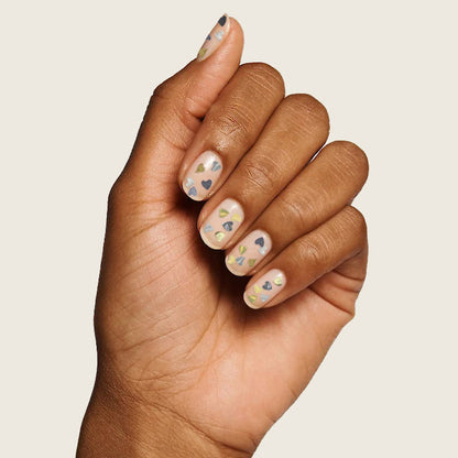 Hand with short nails decorated with colorful heart confetti glitter using Biggest Fan polish by Olive and June