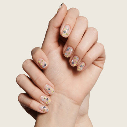 Hand with short nails decorated with silver and gold heart confetti glitter using Biggest Fan polish by Olive and June