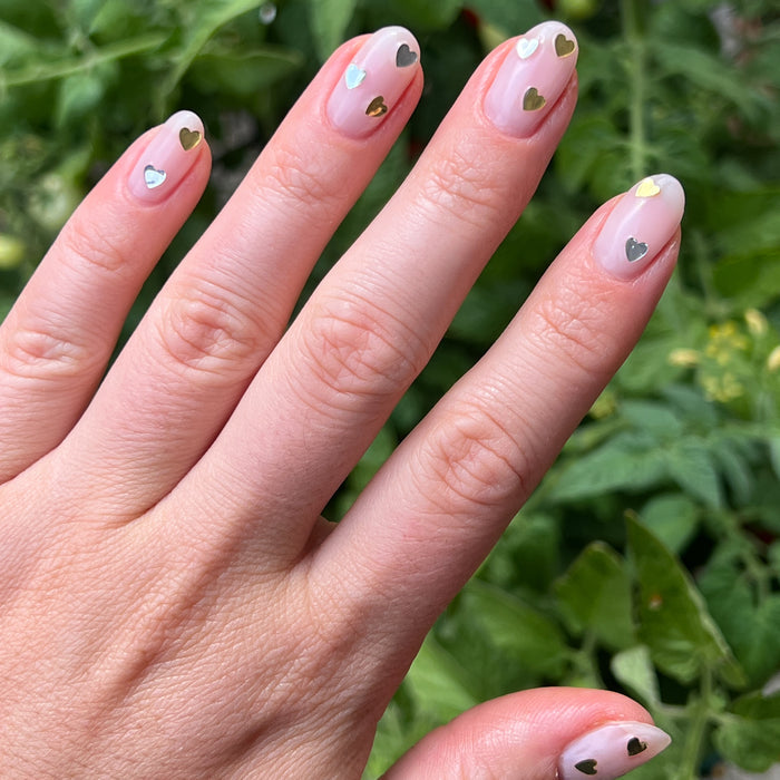 Hand with short natural nails decorated with silver and gold heart confetti using Biggest Fan polish by Olive and June