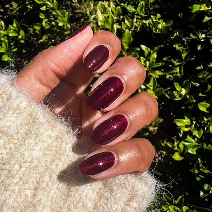 Hand with Bittersweet Cherry manicure in deep cherry polish with subtle shimmer on natural skin tone outdoors