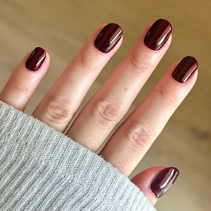 Hand with Bittersweet Cherry manicure in rich dark cherry polish on natural skin tone wearing light gray sweater sleeve