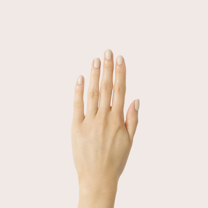 Hand with smooth manicure in light almond cream shade Chemistry nail polish on pale neutral background