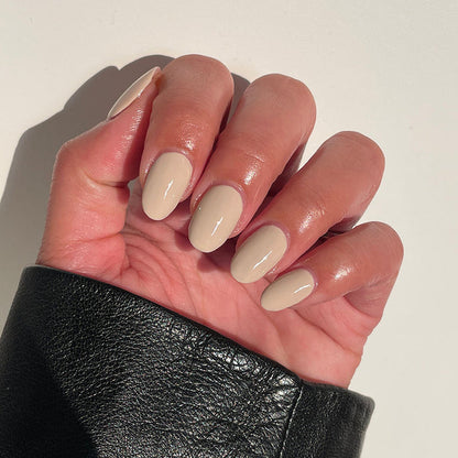 Hand with glossy Chemistry nail polish in light almond cream shade on a natural skin tone against a white background
