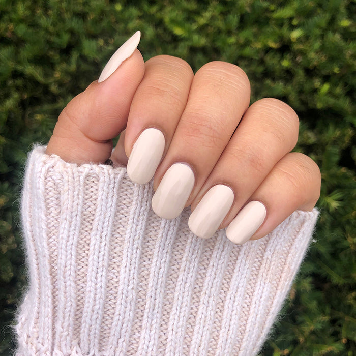 Hand with smooth manicure wearing Chemistry nail polish in soft light almond cream shade outdoors with knitted sweater cuff