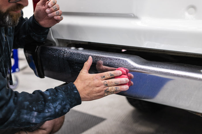 Person cleaning a car bumper with a KochChemie Abrasive Clay Bar.