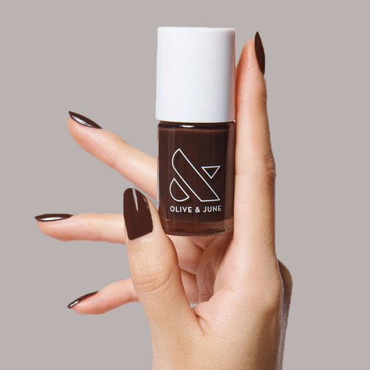 Hand holding Olive and June CN nail polish bottle with nails painted in silky sable brown long-lasting mani color
