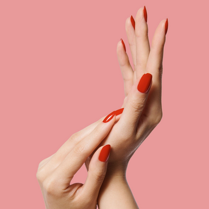 Hands with nails painted bright cherry red using CV polish by Olive and June on a soft pink background