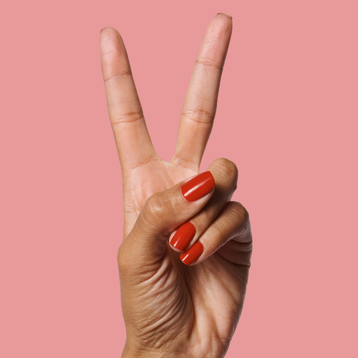 Hand showing nails painted in bright cherry red CV polish by Olive and June against a muted pink background