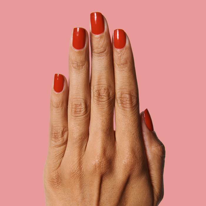 Hand with nails painted in warm bright cherry red using CV nail polish against a muted pink background