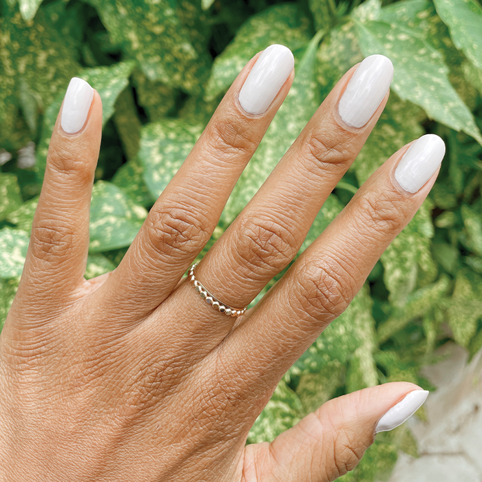 Hand with medium-toned skin wearing ECC polish in cool white grey shade shown against green foliage background