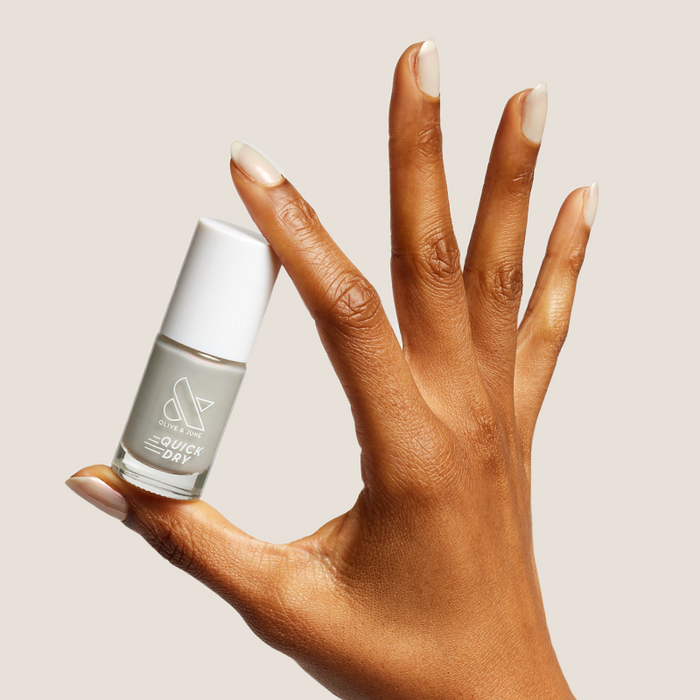 Elevator quick dry polish bottle held by hand with neutral milky grey manicure nails for at home mani
