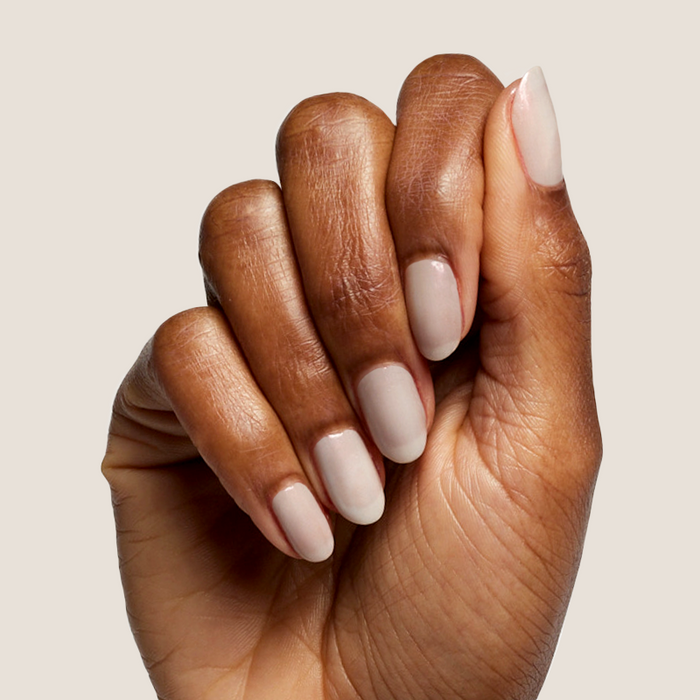 Hand with natural skin tone nails painted in iridescent milky grey Elevator quick dry polish for at home manicure