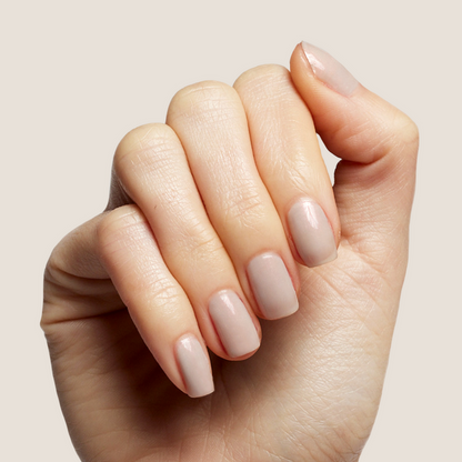 Hand with natural skin tone nails painted in soft iridescent milky grey Elevator quick dry polish for a clean mani