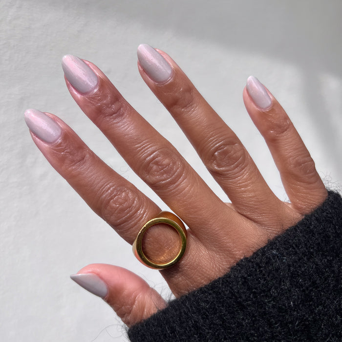 Hand with warm skin tone wearing gold ring and Elevator quick dry polish in iridescent milky grey for polished mani