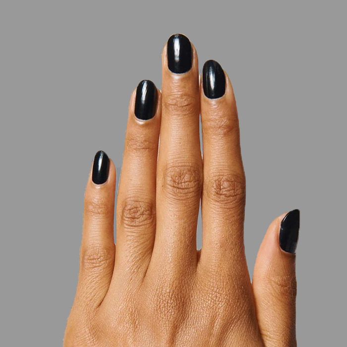 Hand with nails painted in deep black polish showing a smooth E+M manicure by Olive and June on gray background