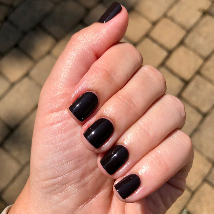 Hand displaying glossy nails polished with E+M deep black long-lasting nail polish by Olive and June