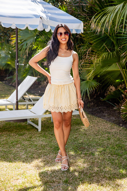Woman in a white top and yellow skirt standing outdoors with palm trees in the background