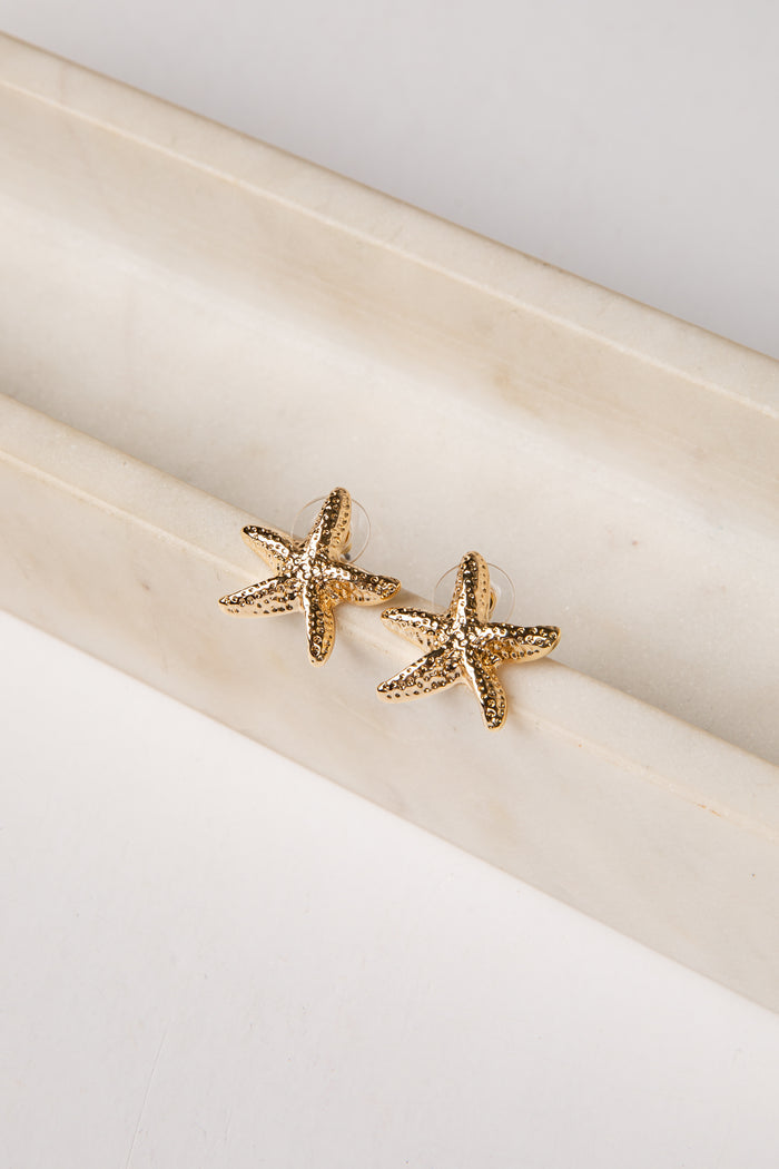 Gold starfish earrings on a white surface