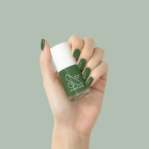 Hand holding a bottle of Geometry polish with neatly manicured nails in classic hunter green shade