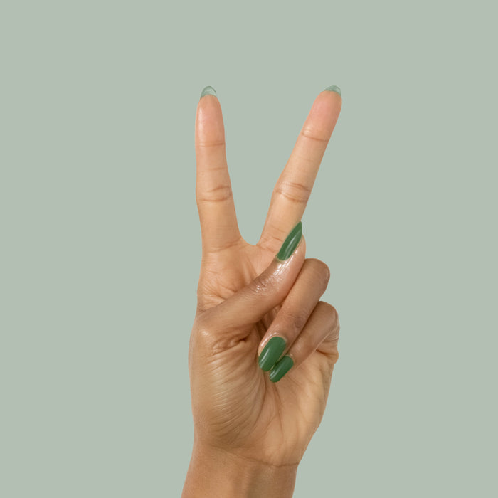 Hand with Geometry polish in classic hunter green on neatly manicured nails against a soft green backdrop