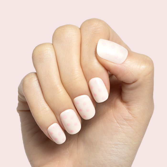 Heart Shower | Extra Short | Squoval - Tab Press-On soft neutral nails with delicate pink hearts on hand against light pink background