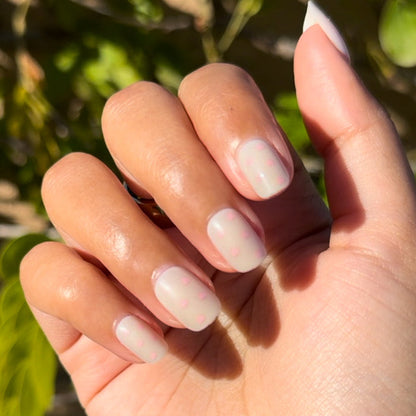 Heart Shower | Extra Short | Squoval - Tab Press-On nails with subtle pink hearts on neutral base shown on hand outdoors in sunlight