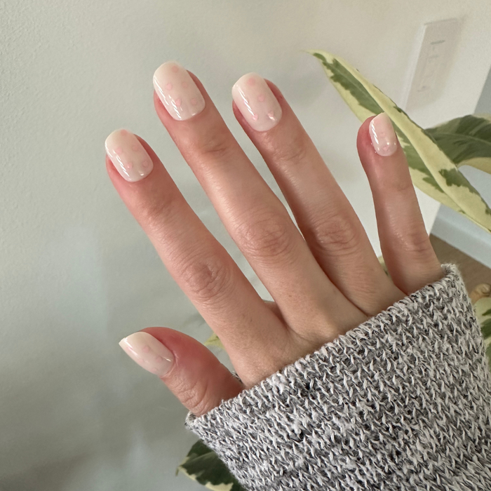Heart Shower | Extra Short | Squoval - Tab Press-On neutral toned press-on nails with soft pink heart patterns on hand in cozy gray sweater