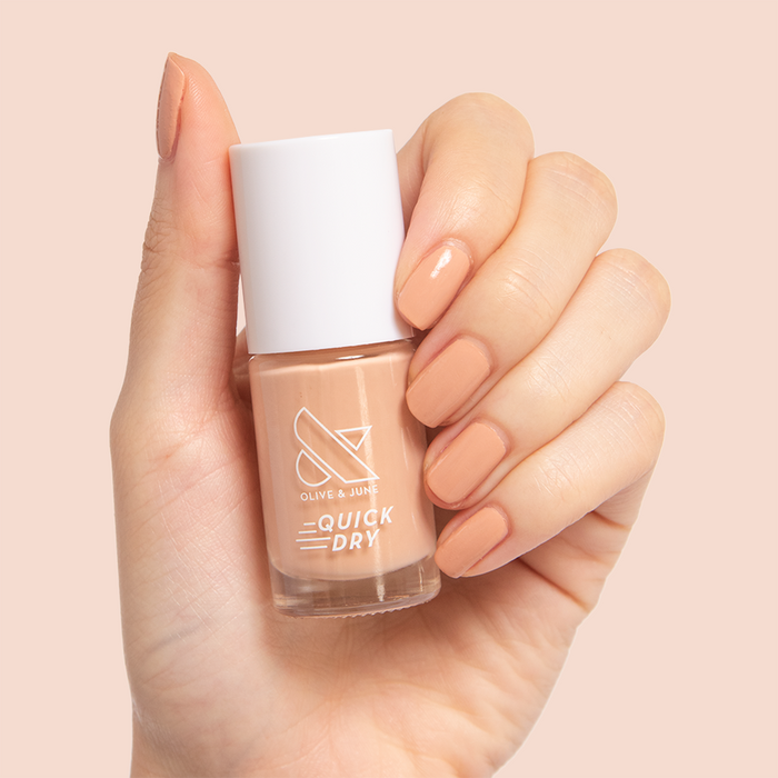 Hand holding Olive and June Howdy nail polish bottle with nails painted in warm neutral beige mani shade
