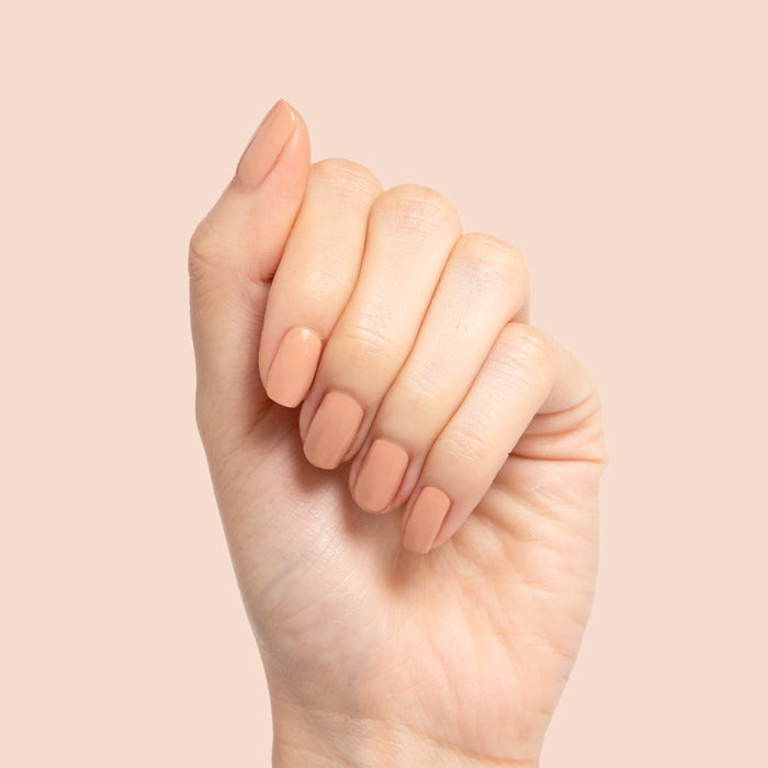 Hand with nails painted in smooth neutral beige Howdy polish showing a glossy manicure on pale background