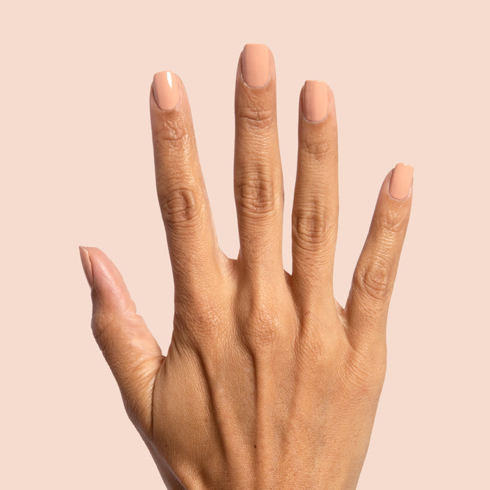 Hand displaying smooth neutral beige nails painted with Howdy polish against a soft peach background