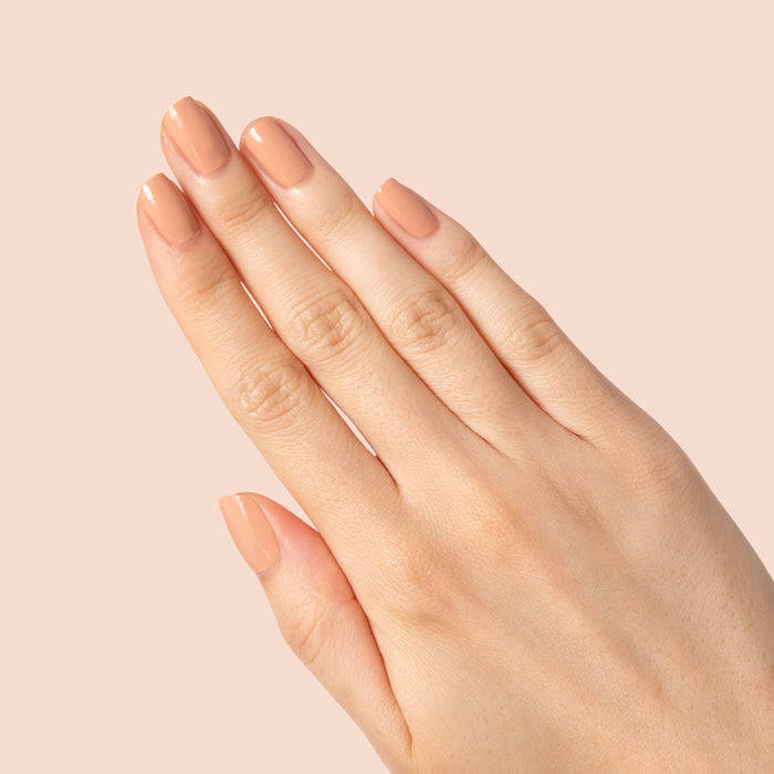 Hand with nails painted in warm neutral beige Howdy polish showing a glossy manicure on soft peach background