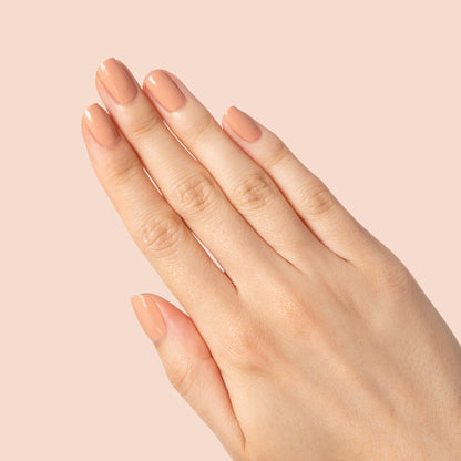 Hand with nails painted in warm neutral beige Howdy polish showing a glossy manicure on soft peach background