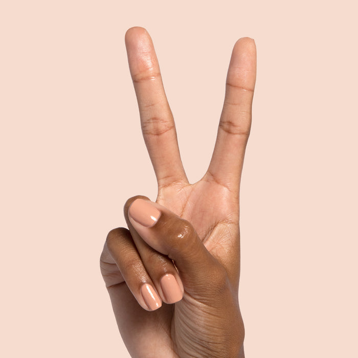 Hand with nails painted in Howdy neutral beige polish holding fingers in a peace sign on peach background